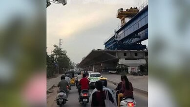 Busy street scene with motorcycles and pedestrians near a large construction site and elevated railway in.