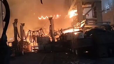 Fire engulfing industrial equipment at night, with intense flames and smoke rising, causing significant d.