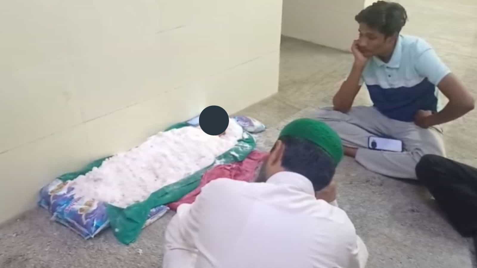 A young man praying on the floor with a green cap, facing a makeshift prayer area with a pillow and white.