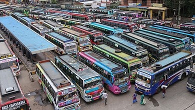 A busy bus station with numerous colourful buses parked and people walking around.