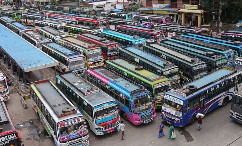A busy bus station with numerous colourful buses parked and people walking around.