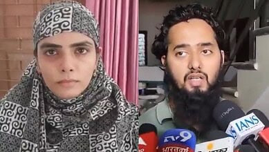 A woman wearing a patterned headscarf and a man with a beard speaking to the media with multiple micropho.