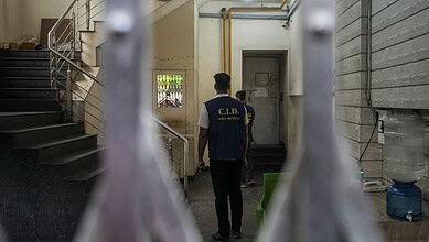 Young man in C.I.D. uniform walking through an indoor corridor with stairs and a water cooler.