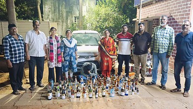A woman kneeling among bottles of illegal alcohol seized by authorities in an outdoor setting.