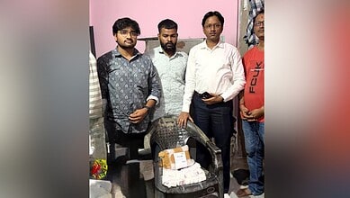 Group of men standing around a desk with a stack of cash and a mobile phone in an indoor setting.