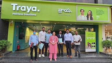A woman and six men standing outside a hair salon with a green signboard that reads "Traya Hairloss Solut.