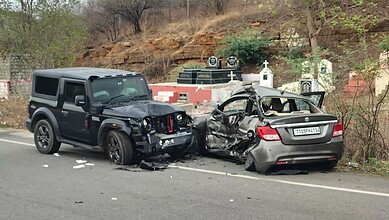 Damaged black SUV and silver sedan after a collision on the roadside, with debris and a hilly background.