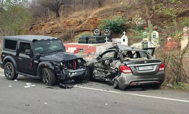 Damaged black SUV and silver sedan after a collision on the roadside, with debris and a hilly background.