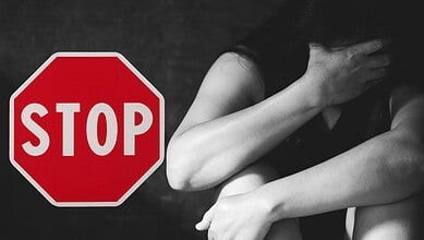 Stop sign on a dark background with a woman covering her face, symbolising distress or emotional struggle.