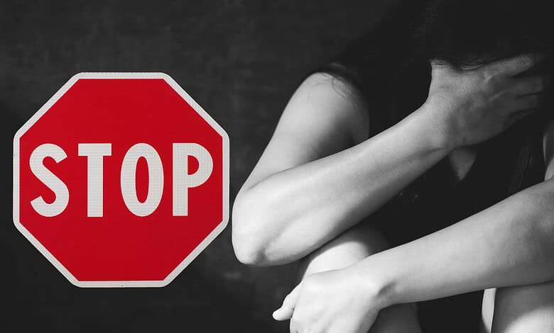 Stop sign on a dark background with a woman covering her face, symbolising distress or emotional struggle.