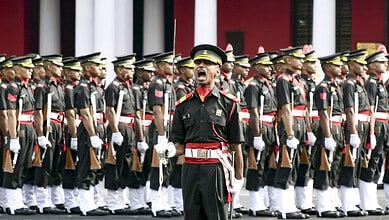 A soldier leading a military parade with uniformed personnel standing in formation behind him.