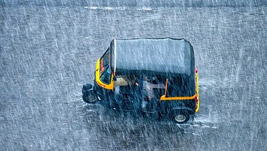 Small auto rickshaw driving through heavy rain on a wet street in India.