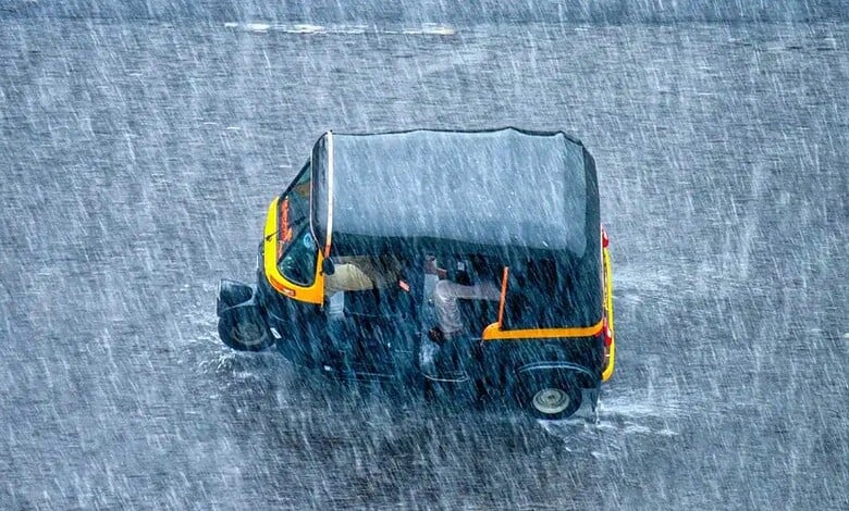 Small auto rickshaw driving through heavy rain on a wet street in India.