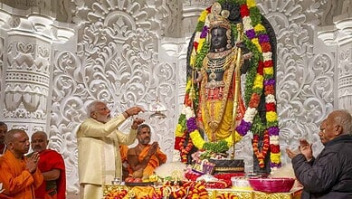 A Hindu priest performing a ritual in front of a decorated black stone deity statue adorned with flowers.