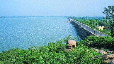 Serene view of a long bridge over a calm water body with lush greenery and clear blue sky in the backgrou.