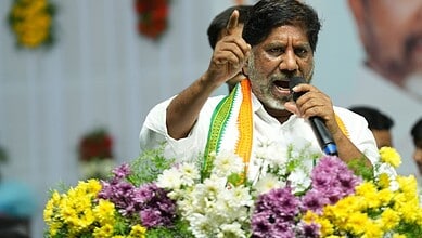 Politician speaking passionately at a public event with flowers in the background.