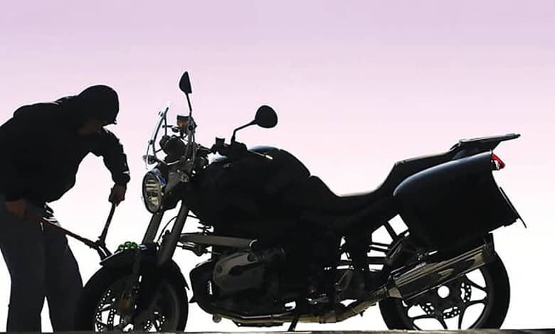 Silhouette of a person with a motorcycle against a pink and purple sky at sunset.