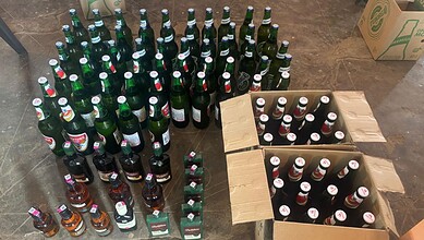 Bottles of alcohol arranged in a semi-circle with some in cardboard boxes on the ground.