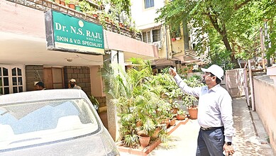 Man in white shirt and cap watering plants outside a clinic in Hyderabad.