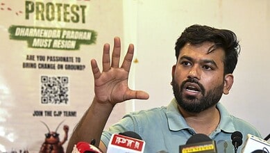 Man speaking at a press conference with protest poster in background.