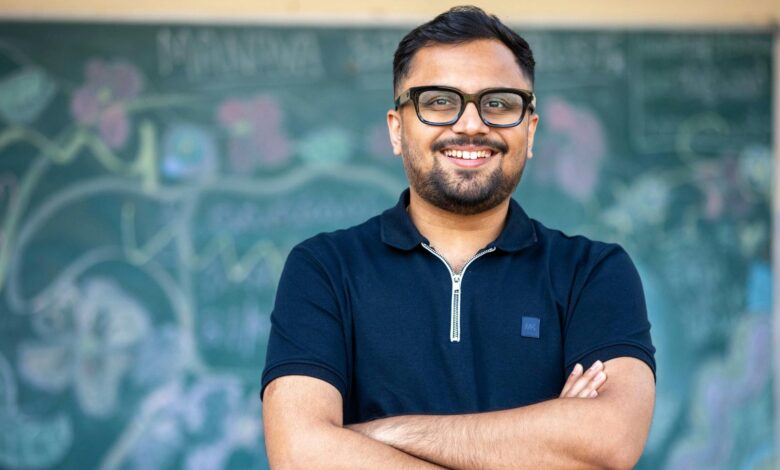 Smiling male teacher in front of a chalkboard with drawings and equations.
