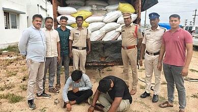 Group of men, including police officers, standing outdoors near a truck loaded with bags.