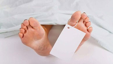 Close-up of a person's feet with a blank white tag attached, on a white bed.
