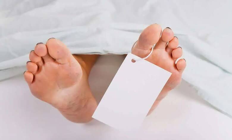 Close-up of a person's feet with a blank white tag attached, on a white bed.