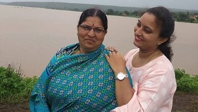 Two women standing by a riverbank, smiling and embracing each other.
