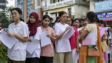 Students waiting in line for NEET retest at exam centre with security in background.