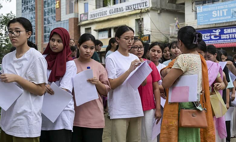 Students waiting in line for NEET retest at exam centre with security in background.