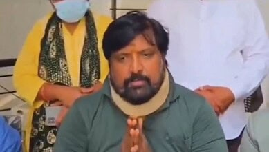 Man speaking with folded hands during a press conference or meeting.