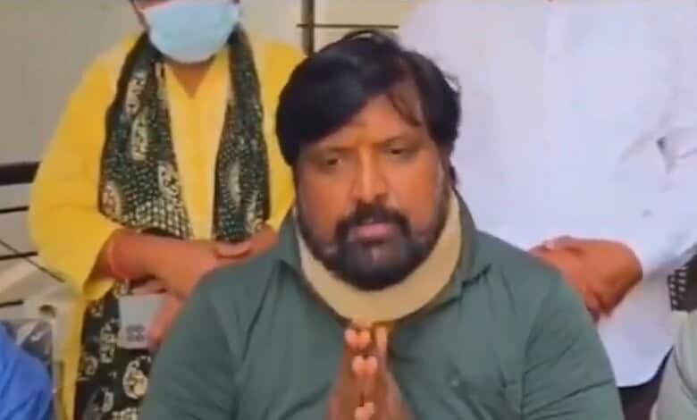 Man speaking with folded hands during a press conference or meeting.