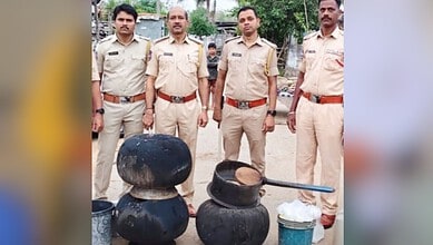 Police officers standing behind seized illegal alcohol bottles in Telangana.