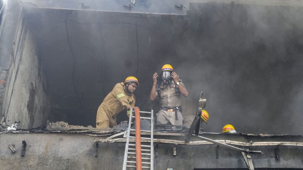 Firefighters inspecting the aftermath of a fire in a building with smoke and charred walls.