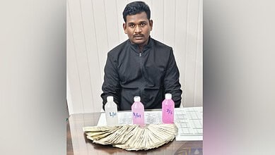 Man sitting at a table with cash and bottles, in front of a white wall.