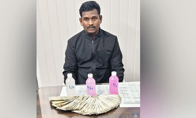 Man sitting at a table with cash and bottles, in front of a white wall.