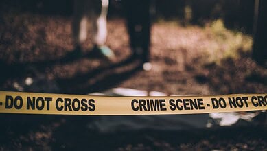Crime scene tape reading 'Do Not Cross' at a dark, wooded area.
