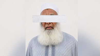 Man with a white beard and traditional white cap, eyes covered with a white strip.