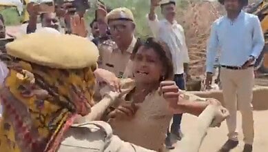 Emotional woman protesting as bulldozers demolish Rajasthan homes, with onlookers nearby.
