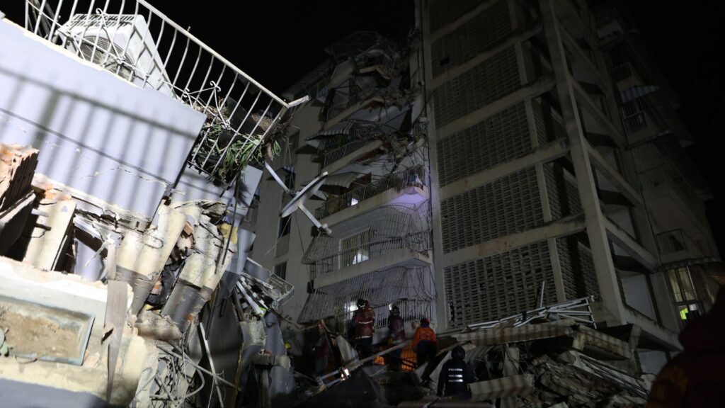 Nighttime scene of collapsed building and rescue workers in Venezuela after earthquake.
