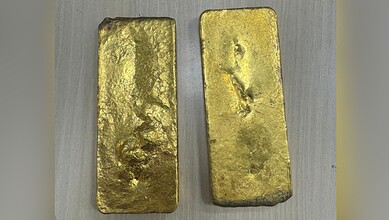 Two gold bars with rough surfaces and uneven edges on a metallic surface.