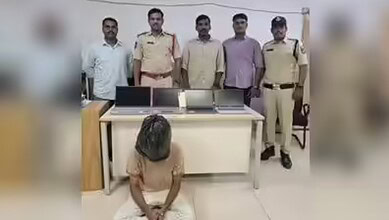 Police officers and a woman in a room with laptops and a black bag on the desk.
