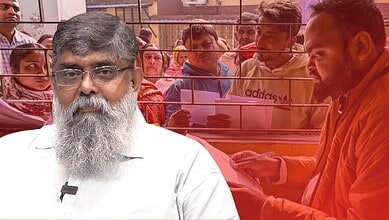 A man with a beard and glasses speaking to a crowd behind a glass barrier.