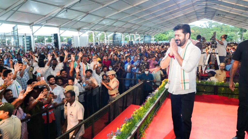 Revanth Reddy addressing a large crowd at a political rally under a canopy.