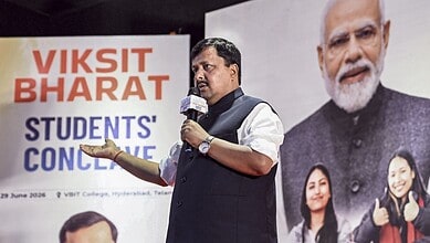 BJP chief addressing a crowd at a political event with a large Modi poster in the background.