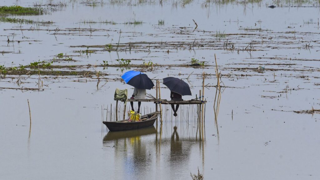 Flooded field with two people on a wooden raft during heavy monsoon rains in Arunachal Pradesh.