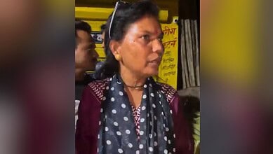 Woman speaking at a public event with yellow banners in the background.