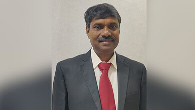 Professional portrait of a man in a suit with a red tie against a plain background.