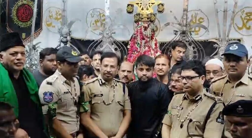 Police officers and a man in black pose with a decorated religious figure during a public event.